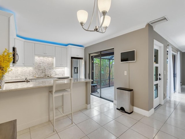 kitchen featuring appliances with stainless steel finishes, pendant lighting, white cabinetry, ornamental molding, and light stone countertops