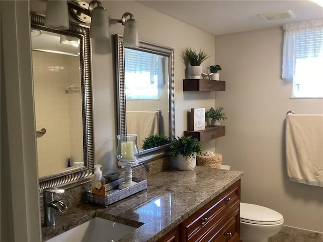 bathroom featuring vanity, toilet, a healthy amount of sunlight, and tiled shower