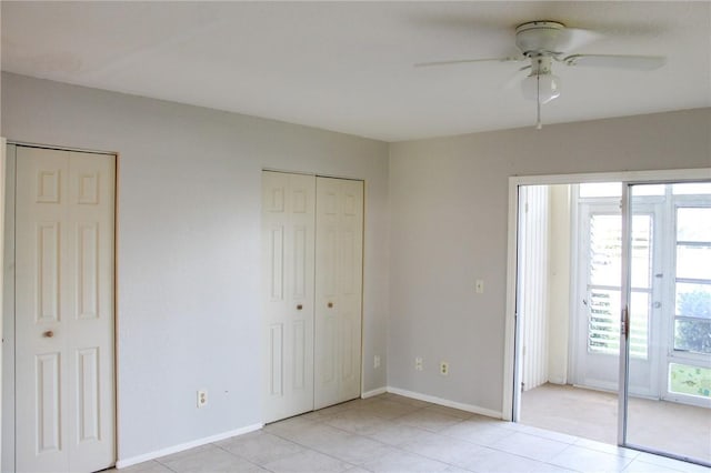 unfurnished bedroom featuring a ceiling fan, light tile patterned floors, baseboards, and two closets