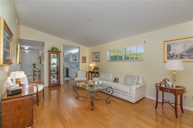 living room featuring light hardwood / wood-style floors, sink, and vaulted ceiling