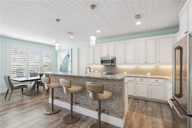 kitchen featuring stainless steel appliances, hardwood / wood-style flooring, a center island with sink, decorative light fixtures, and white cabinets