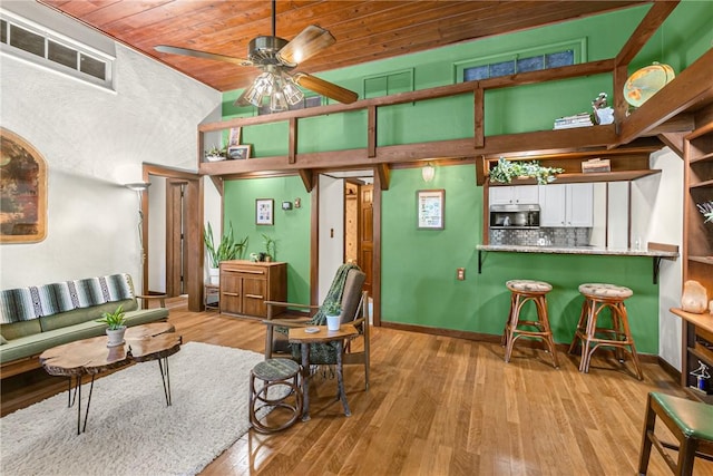 living area featuring a ceiling fan, wood ceiling, baseboards, and wood finished floors