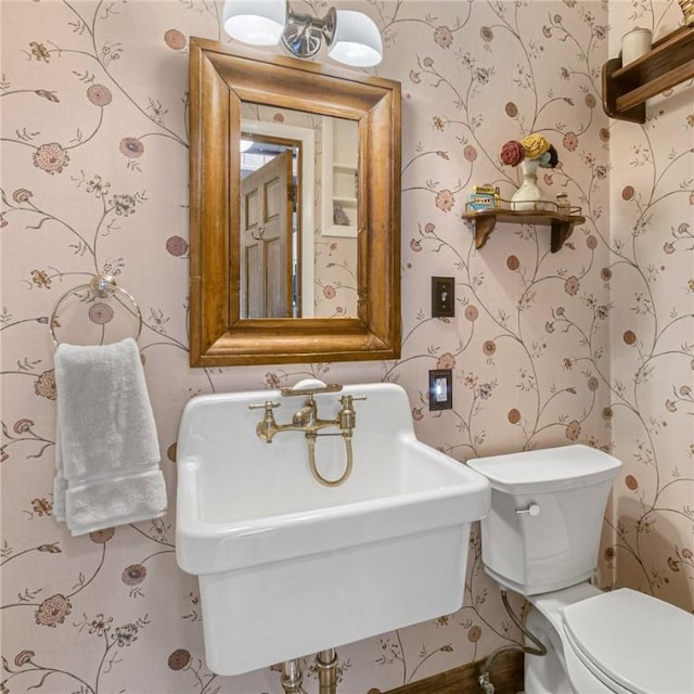 half bathroom featuring a sink, toilet, and wallpapered walls