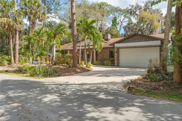 ranch-style home with driveway, brick siding, a chimney, and an attached garage