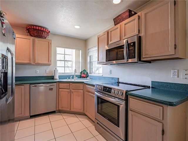 kitchen with light brown cabinets, a sink, dark countertops, appliances with stainless steel finishes, and light tile patterned floors