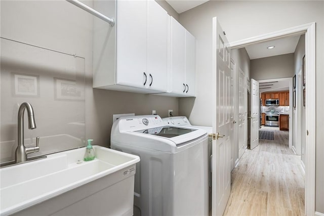 clothes washing area with cabinets, light wood-type flooring, and sink