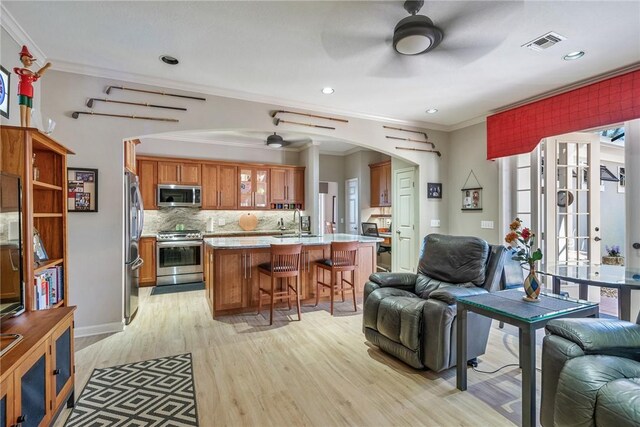 kitchen with a kitchen bar, stainless steel appliances, crown molding, sink, and light hardwood / wood-style floors