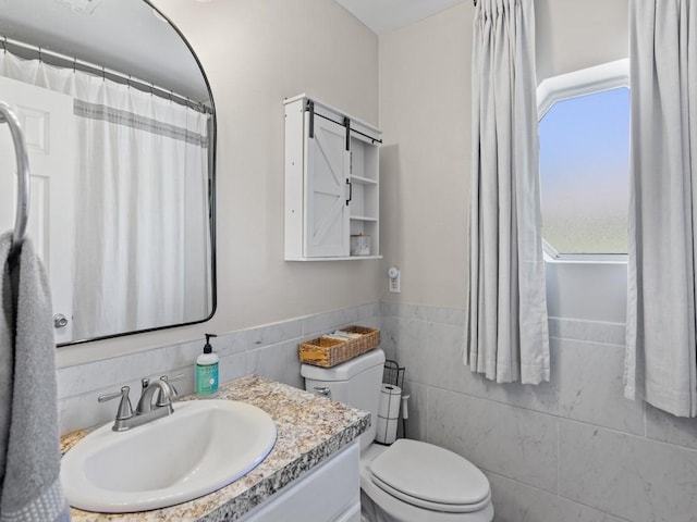 bathroom with tile walls, toilet, vanity, and a wainscoted wall