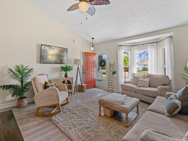 living room with vaulted ceiling, light wood-style floors, baseboards, a textured ceiling, and ceiling fan