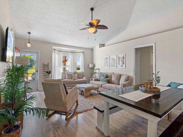 living room featuring vaulted ceiling, light wood-style flooring, a textured ceiling, and a ceiling fan