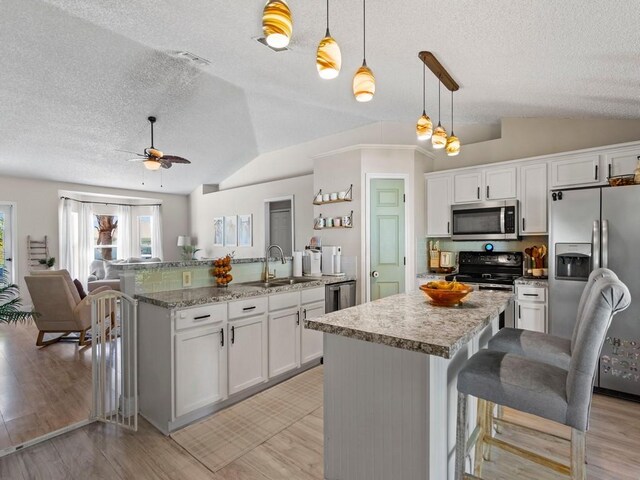 kitchen featuring stainless steel appliances, a sink, a textured ceiling, lofted ceiling, and a breakfast bar