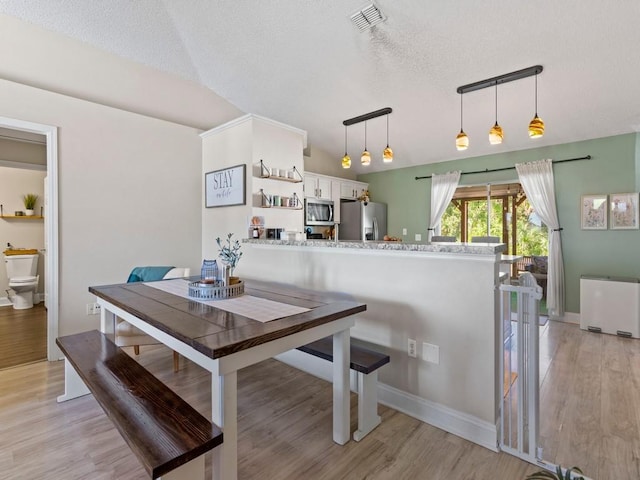 dining room featuring a textured ceiling, radiator heating unit, visible vents, and light wood finished floors