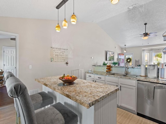 kitchen featuring vaulted ceiling, stainless steel dishwasher, a sink, a textured ceiling, and ceiling fan