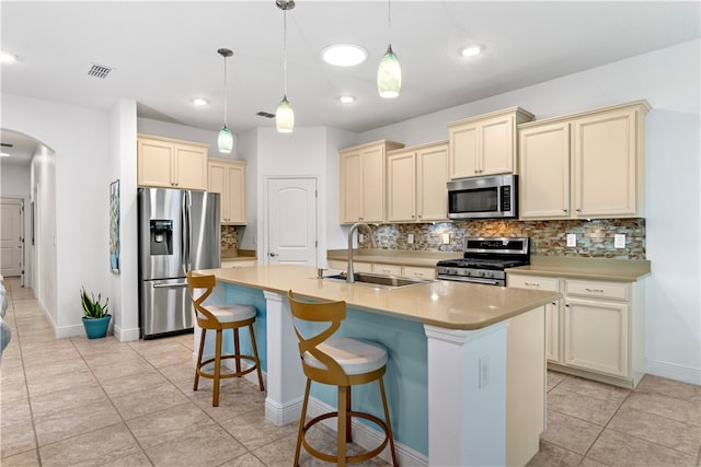 kitchen with sink, an island with sink, pendant lighting, appliances with stainless steel finishes, and cream cabinetry