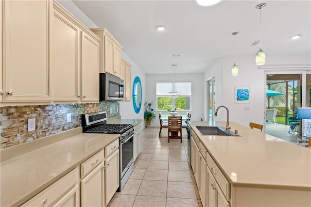 kitchen featuring a center island with sink, stainless steel appliances, light tile patterned floors, hanging light fixtures, and sink