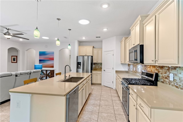 kitchen with a center island with sink, stainless steel appliances, backsplash, hanging light fixtures, and sink