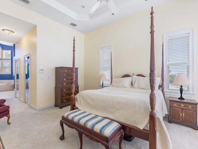 bedroom featuring ceiling fan, crown molding, ensuite bathroom, a tray ceiling, and light carpet