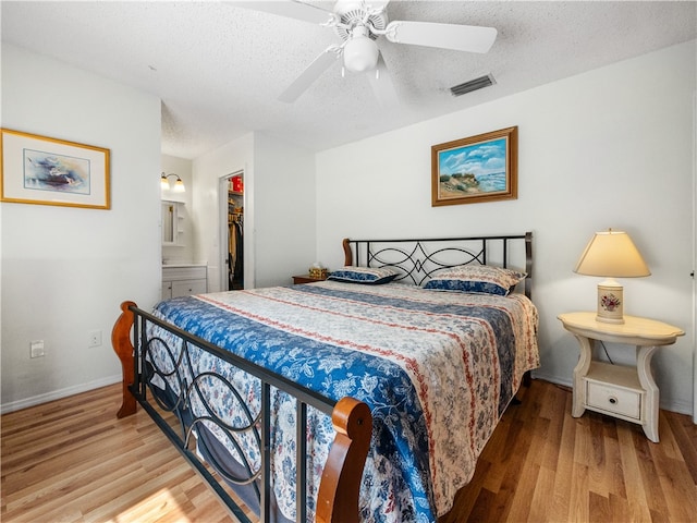 bedroom featuring a closet, a spacious closet, light wood-type flooring, a textured ceiling, and ceiling fan