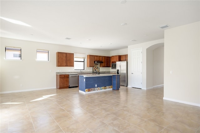 kitchen featuring a center island, brown cabinets, stainless steel appliances, light countertops, and visible vents