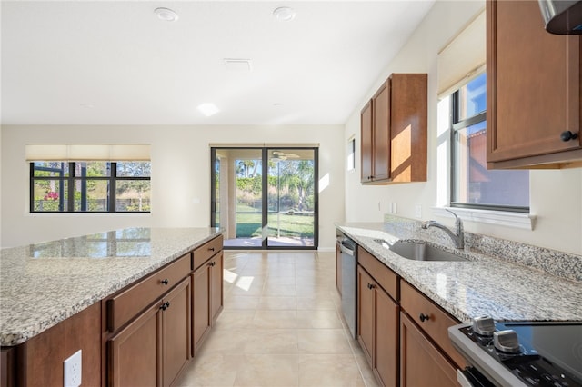 kitchen with stainless steel dishwasher, brown cabinetry, a sink, light stone countertops, and range