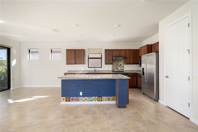 kitchen featuring visible vents, a kitchen island, light stone countertops, stainless steel appliances, and under cabinet range hood