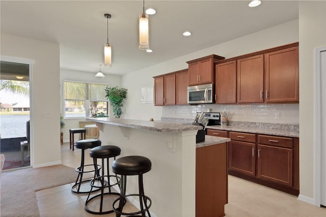 kitchen featuring backsplash, stainless steel appliances, a kitchen breakfast bar, light stone counters, and decorative light fixtures