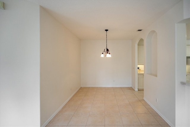 tiled spare room with an inviting chandelier