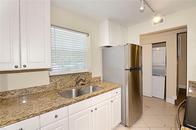 kitchen featuring stainless steel refrigerator, light stone countertops, sink, white cabinets, and stacked washer / drying machine