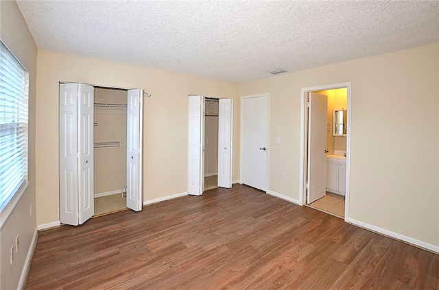 unfurnished bedroom with multiple closets, a textured ceiling, hardwood / wood-style floors, and ensuite bathroom