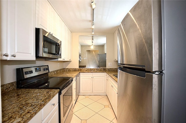 kitchen with light tile patterned flooring, white cabinetry, appliances with stainless steel finishes, rail lighting, and dark stone countertops