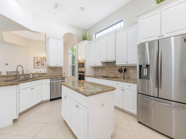 kitchen featuring stainless steel appliances, dark stone counters, plenty of natural light, and white cabinets