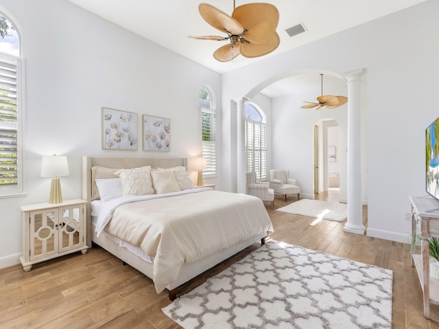 bedroom featuring ornate columns, light wood-type flooring, and multiple windows