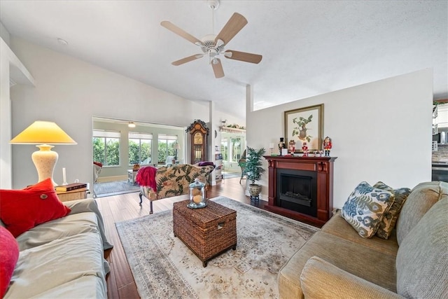 living area with ceiling fan, a fireplace, lofted ceiling, and wood finished floors