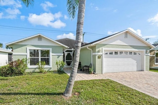 single story home featuring decorative driveway, a front lawn, an attached garage, and stucco siding