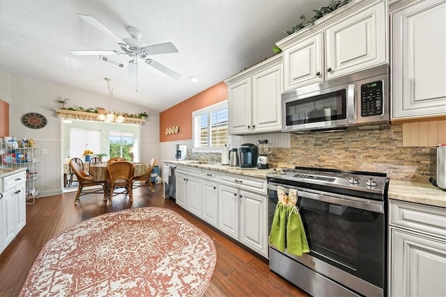 kitchen featuring stainless steel appliances, a wainscoted wall, dark wood-style flooring, and vaulted ceiling