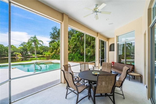 sunroom / solarium with a ceiling fan, a hot tub, a water view, and view of scattered trees