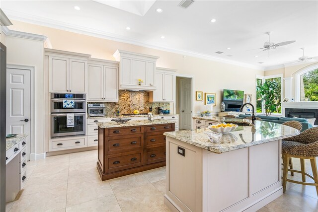 kitchen with light stone counters, a breakfast bar area, ornamental molding, a spacious island, and appliances with stainless steel finishes