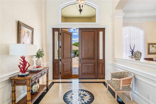 entrance foyer with a decorative wall, wainscoting, inlaid floor details, and crown molding