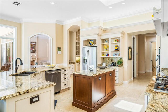 kitchen with ornamental molding, stainless steel appliances, a large island with sink, light stone countertops, and sink