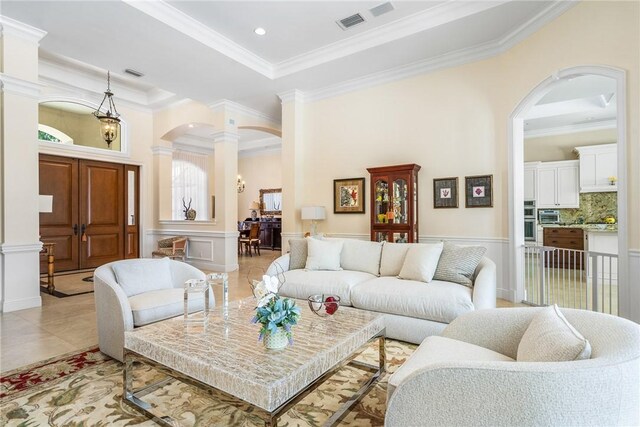 living room with decorative columns, ornamental molding, arched walkways, a decorative wall, and a wainscoted wall