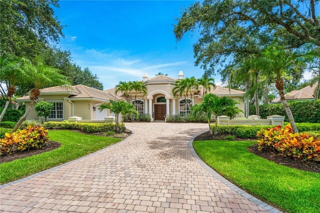mediterranean / spanish house featuring curved driveway, stucco siding, and a front lawn