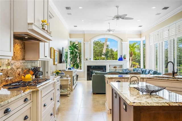 kitchen with a sink, a ceiling fan, light tile patterned flooring, light stone counters, and backsplash