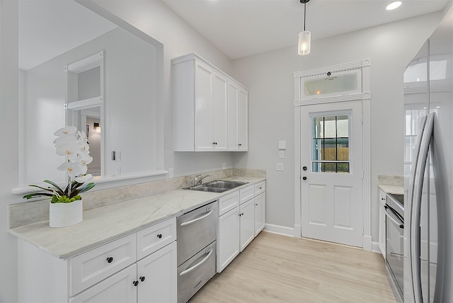 kitchen with stainless steel appliances, white cabinets, sink, light stone countertops, and light wood-type flooring