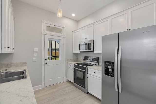 kitchen featuring light wood-type flooring, appliances with stainless steel finishes, hanging light fixtures, sink, and white cabinets