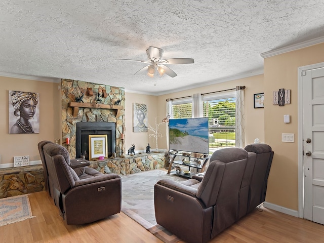 living room with ornamental molding, ceiling fan, a textured ceiling, a fireplace, and light hardwood / wood-style flooring