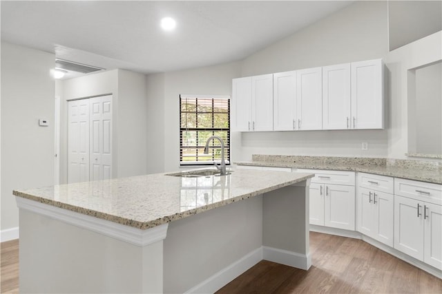 kitchen with vaulted ceiling, white cabinets, light stone counters, and sink