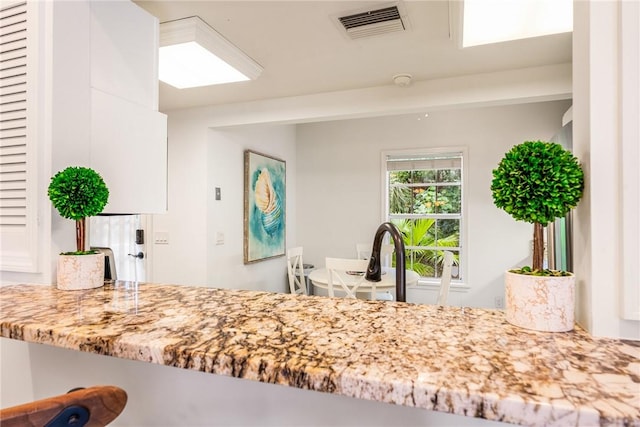 kitchen with white cabinetry, light stone counters, and visible vents