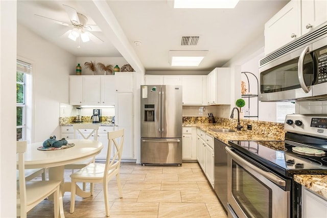 kitchen featuring white cabinetry, light stone counters, stainless steel appliances, and a sink