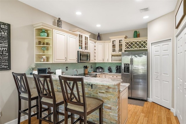 kitchen featuring a breakfast bar, light wood finished floors, open shelves, appliances with stainless steel finishes, and glass insert cabinets