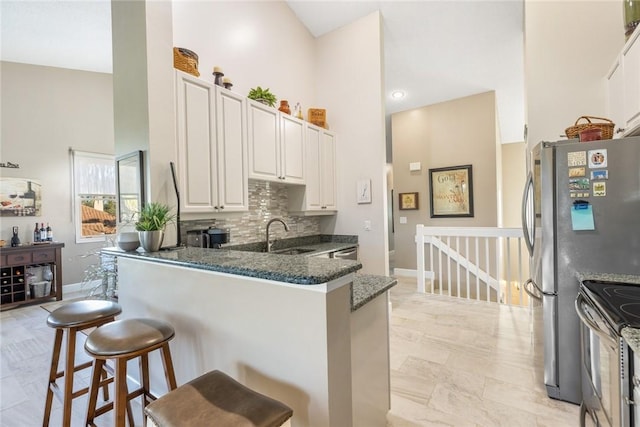 kitchen with kitchen peninsula, a kitchen breakfast bar, dark stone counters, sink, and white cabinets